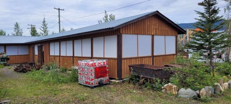 A cubic container filled with water sits in front of a wooden one-storey building.