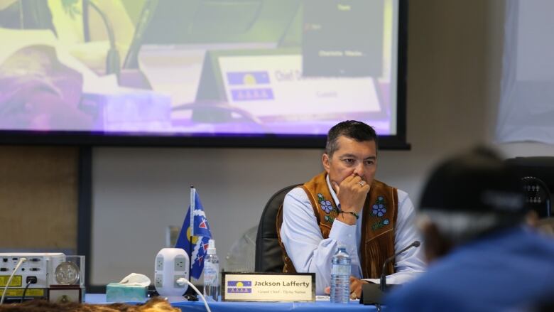 Tch Grand Chief Jackson Lafferty sits at a table with a projector screen behind him in What in mid-July 2022. 