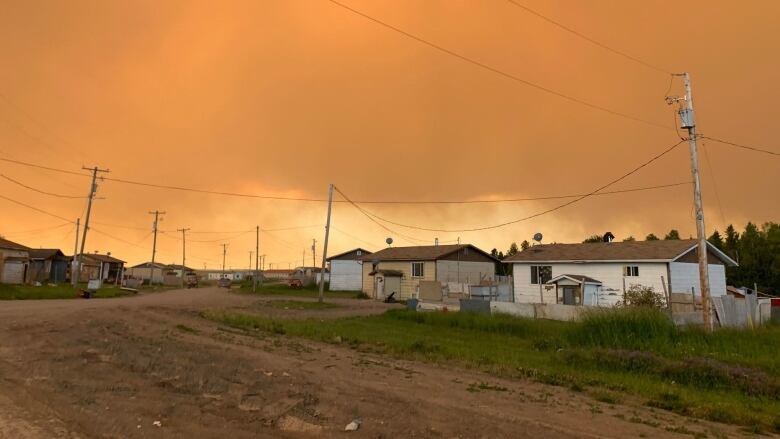 A row of single-storey houses and a dirt road are shown with an orange, smoke-filled sky overhead.