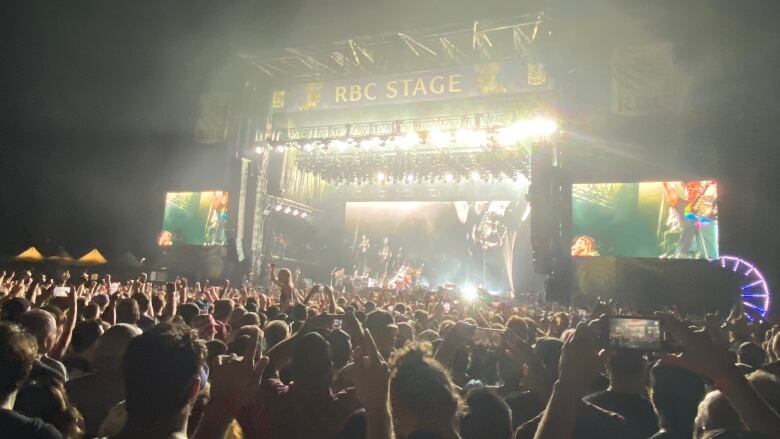 A large crowd of people raise their hands toward a stage where a band plays music.