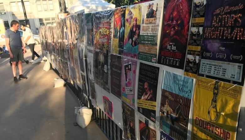  A long poster board is covered with colourful posters advertising Fringe Festival shows.