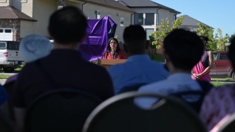 Crowd watches person speak at a podium outside.