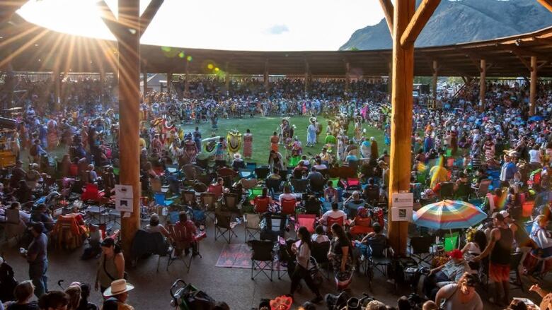 A crowd of people are gathered around a circle, with people wearing Indigenous regalia in the middle.