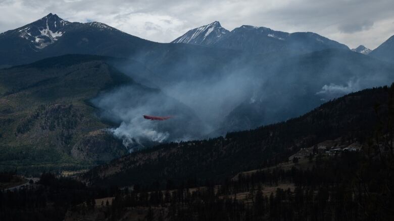 A red plane flies over smoky terrain.