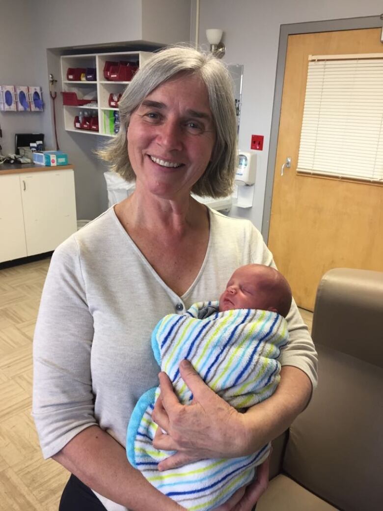 A woman smiles while holding a baby.