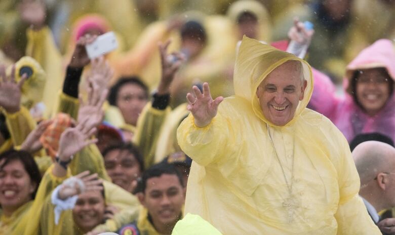 Smiling man wearing a yellow rain poncho surrounded by crowds.