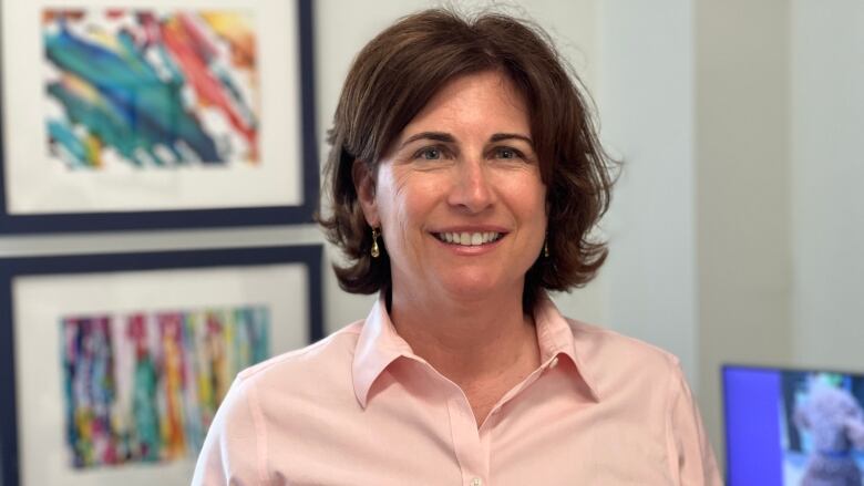 A smiling woman with brown hair wearing a pink shirt.