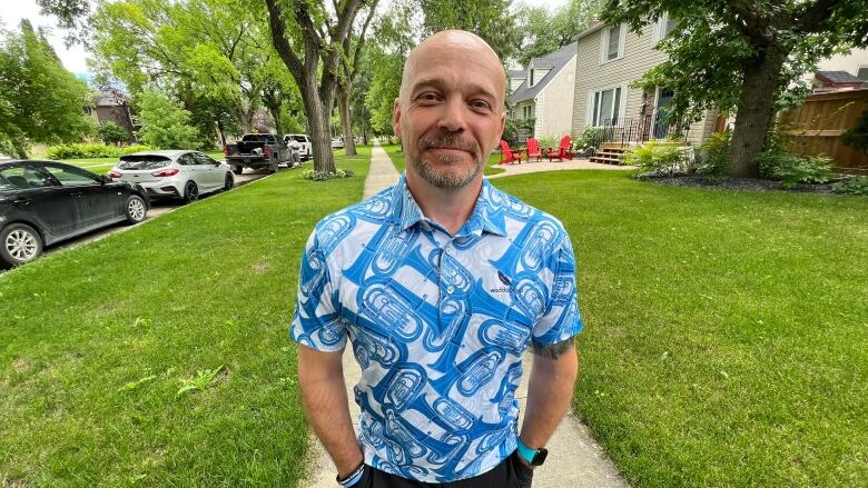 A man stands on a sidewalk wearing a blue-and-white shirt.