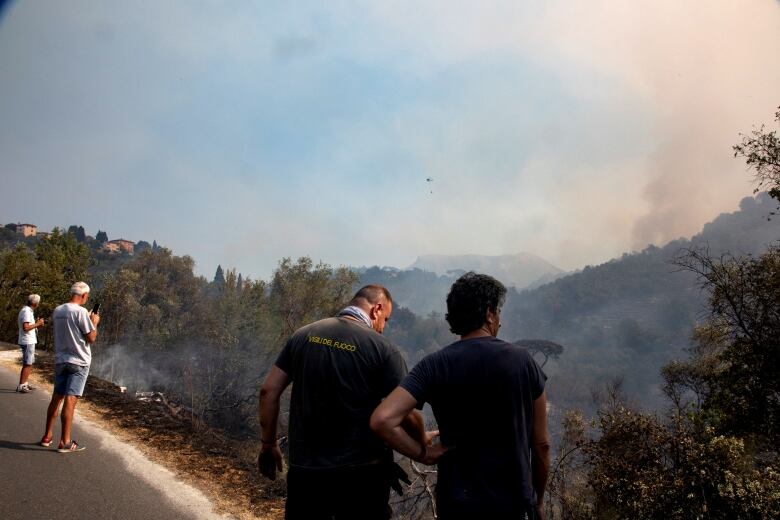 Bystanders watch a wildfire on a hillside.