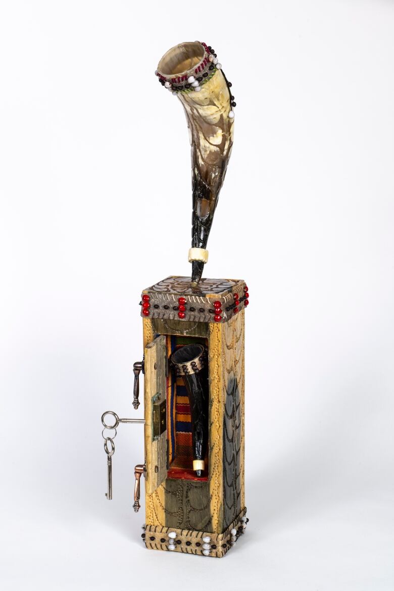 Photo of embellished cow horn musical instrument mounted on an embellished wooden box containing another horn.