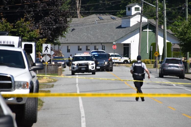 Police vehicles and an officer is seen behind rows of yellow crime tape on a street.