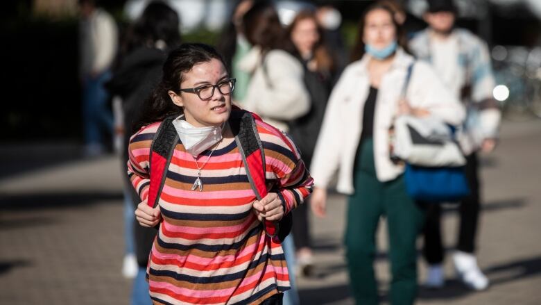 Students wearing backpacks and masks around their necks walk around a campus.