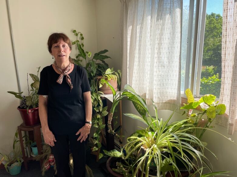 Woman stands by a sunny window, framed by trailing and tall houseplants.