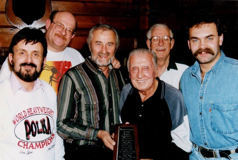 6 older men stand smiling facing the camera