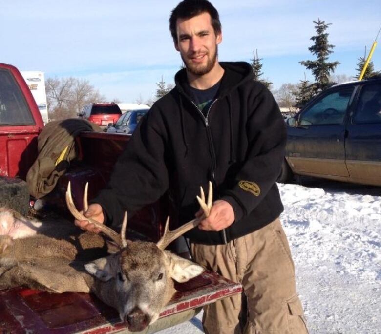 Man holds dead caribou antlers by red pickup truck.