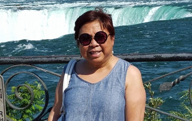 A woman wearing sunglasses poses for the camera in front of a waterfall.