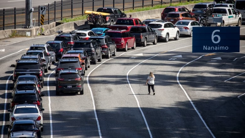 A woman crosses the road as dozens of cars wait in a lineup.