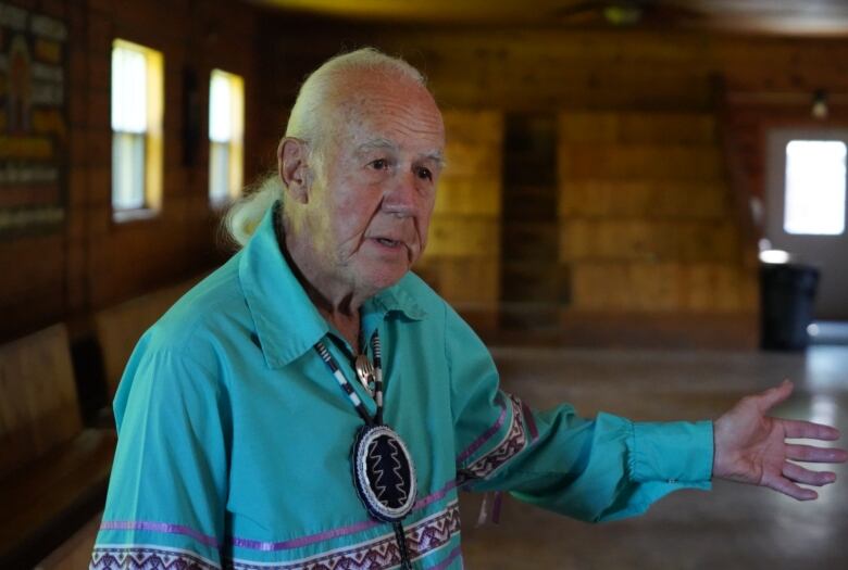 An elderly man stands inside a longhouse. 