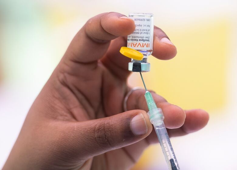 A hand holds the monkeypox vaccine and a syringe.