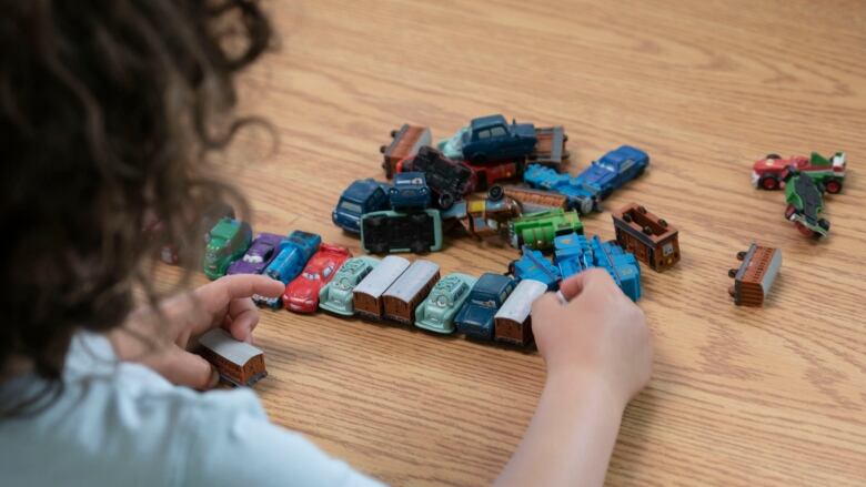 Child facing away from camera plays with small toy cars and trains.