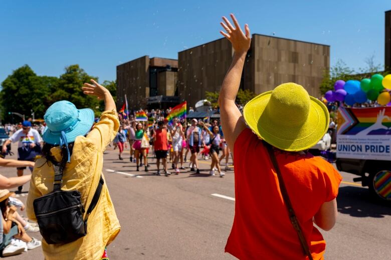 Two women in colourful hats waving to participants at Pride Parade