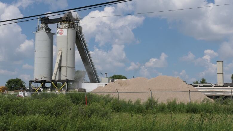 Two tall silos and a mound of gravel are seen at an industrial site.