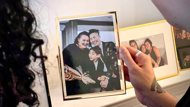 A person holds up a picture with Serene, Stevie, and Noah smiling together.