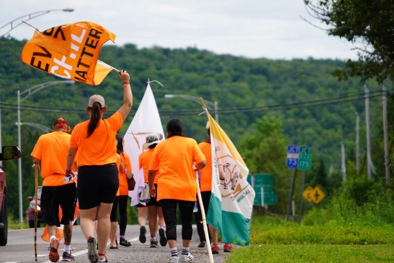 The backs of marchers wearing orange shirts and carrying Every Child Matters banners.