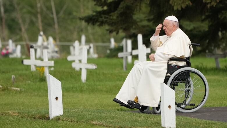 The pope sits in a wheelchair in a cemetery.