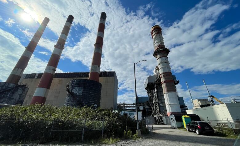 power plant with four large, red-and-white stacks extending into the air with a bright blue sky in the background.