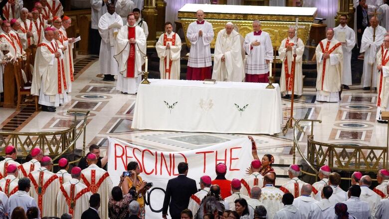 Two people hold up a banner in front of a large crowd in a church.