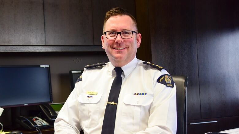 An RCMP officer sits at a desk smiling at the camera.