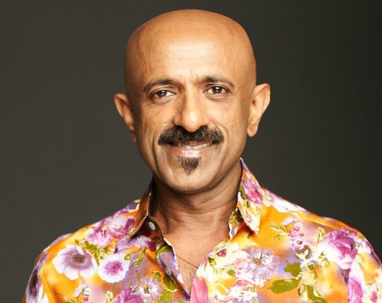 A smiling man with a moustache, wearing a bright coloured shirt. 