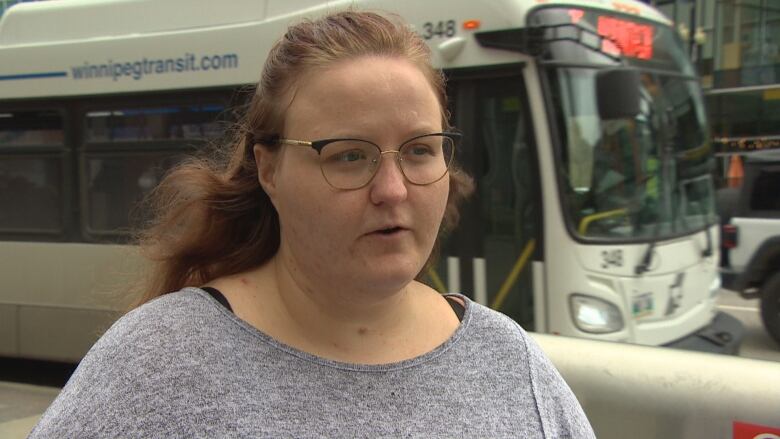 A woman with glasses speaks on a city sidewalk.