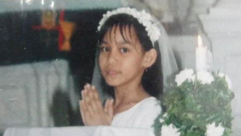 A girl wearing a white gown folds her hands in prayer.