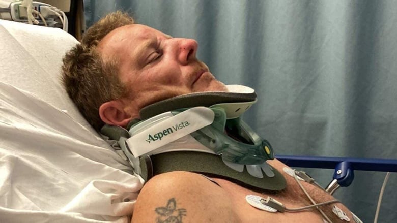 A man lies in a hospital bed with a neck brace.