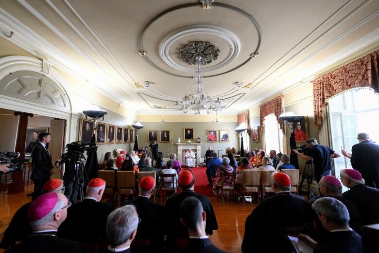 Clergy and Indigneous people are seen in an ornate room.