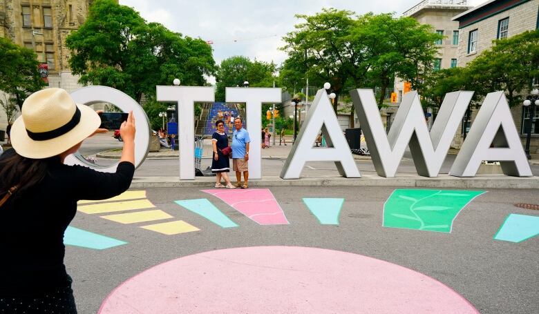 A person takes a photo of two people standing in front of a large 