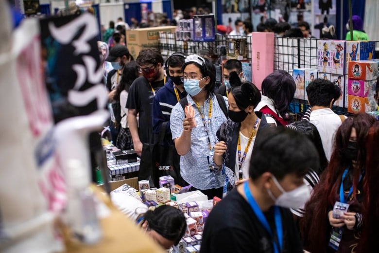 A person points a tiny fan towards another person in the middle of a crowded convention floor.