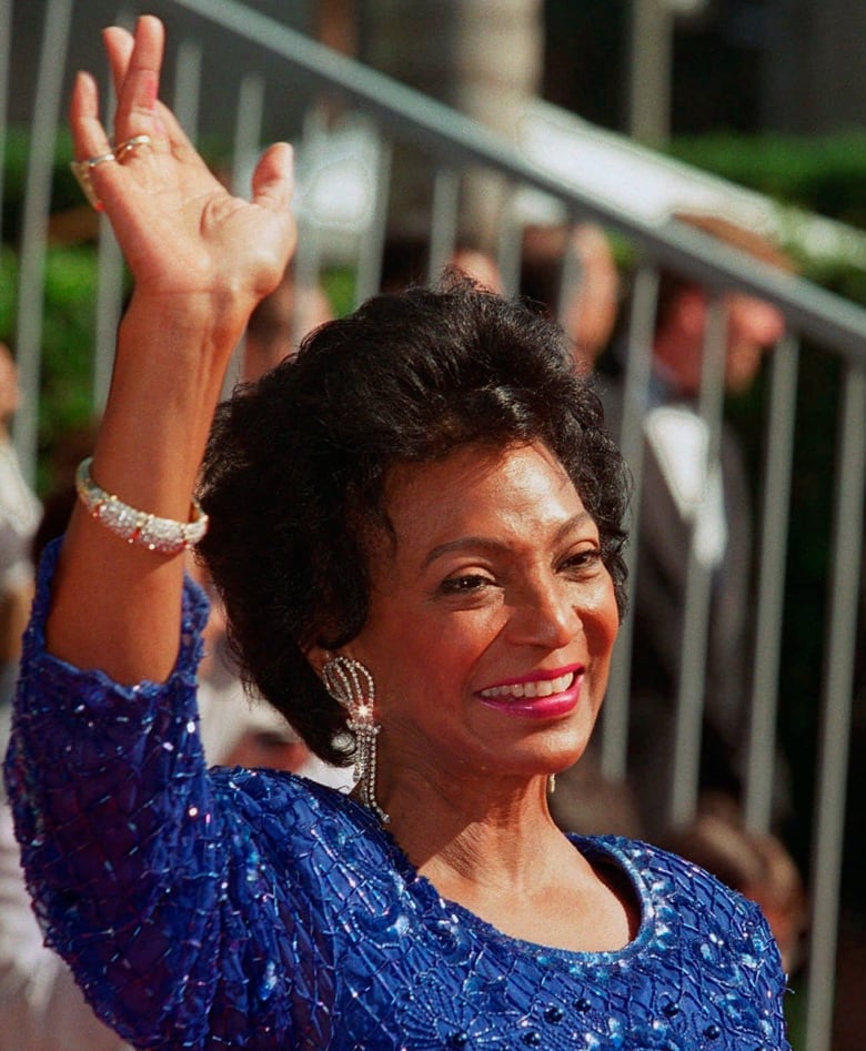 A woman wearing a sparkly blue gown waves