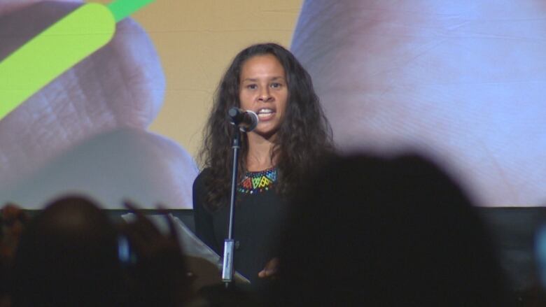 A woman wearing a black top speaking at a mic