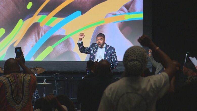 A Black man in a colourful suit holding his fist up