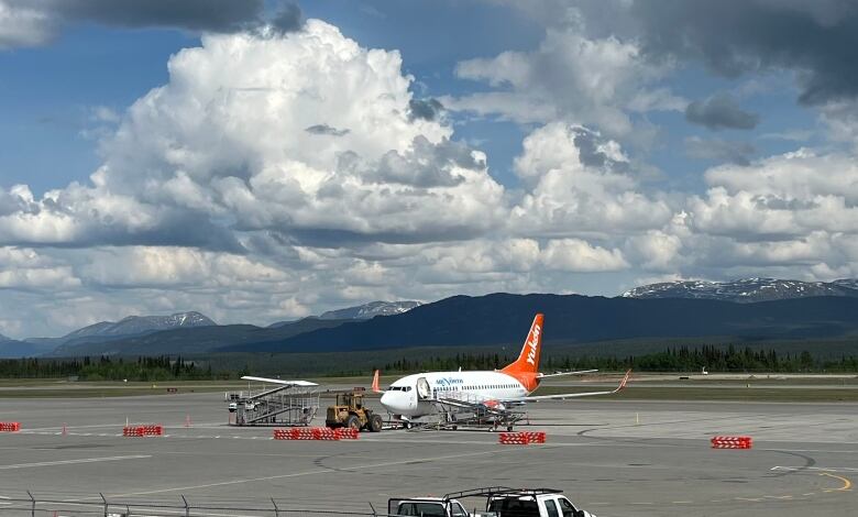 An airplane sits on the tarmac with mountains in the background.