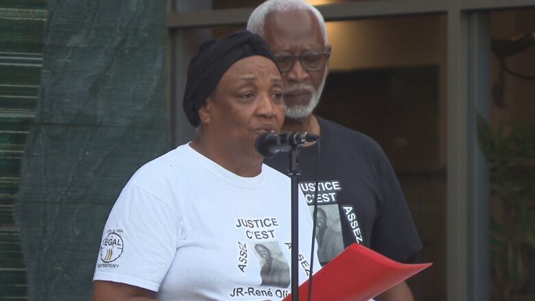 A woman and a man stand in front of a microphone. 