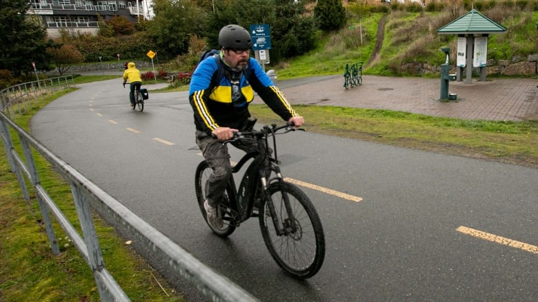 A male cyclist rides an e-bike on a paved trail.