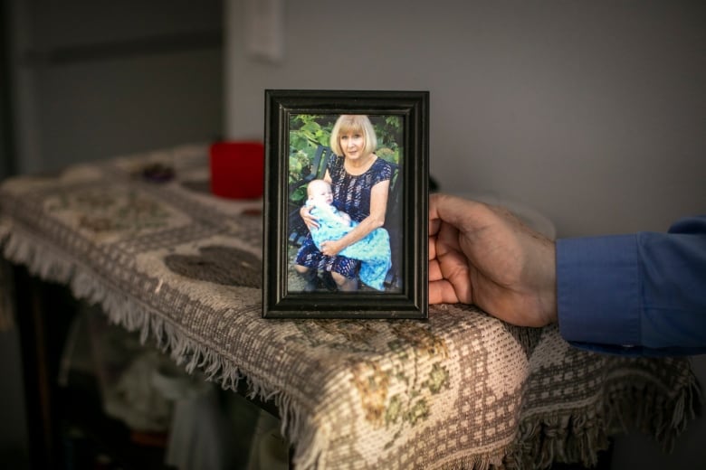 A hand holds a picture of a woman holding a baby wrapped in a blue scarf.