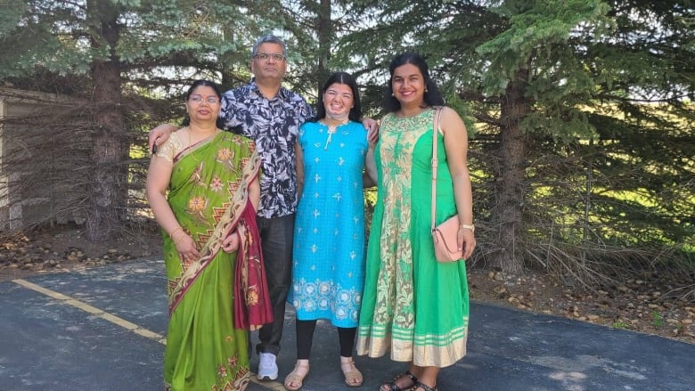 A man and three women dressed in traditional Indian clothes stand on a driveway. 