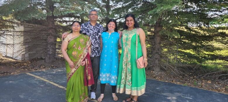 A man and three women dressed in traditional Indian clothes stand on a driveway. 