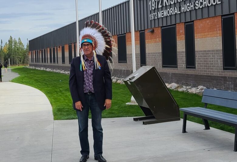 A man wearing a headdress is pictured standing in front of a high school.