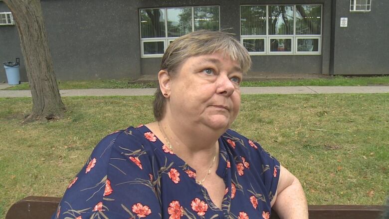 A middle aged woman looking to the right answering a reporter's questions.